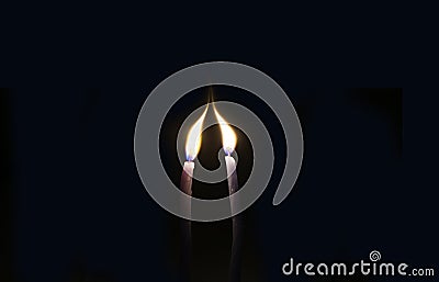 Two thin candles stretch their lights towards each other. The candles are in complete darkness. Stock Photo