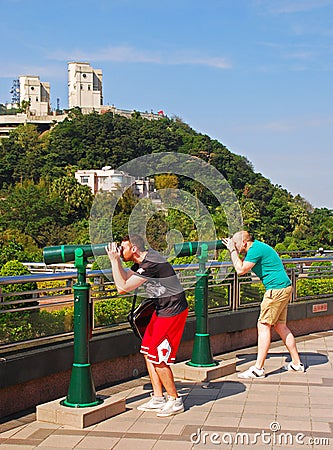 Two tourists using a pair of Green Tourist panoramic telescope at the Peak, Hong Kong Editorial Stock Photo