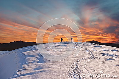 Two tourists walk on a mountain slope to the summit against the backdrop of mystical clouds at sunset Stock Photo