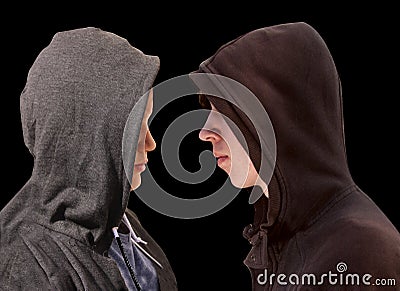 Two troubled teenage boys with black hoodie standing in front of each other in profile isolated on black background - stock Stock Photo