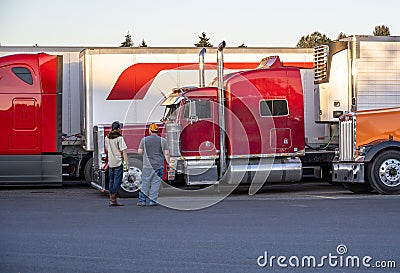 Truck drivers exchange views on the strengths and weaknesses of their big rigs semi trucks standing on truck stop Editorial Stock Photo
