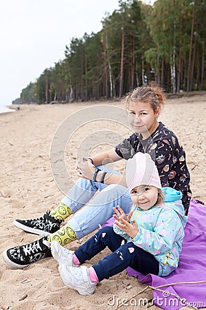 Two and twelve years old children sitting together on empty sandy beach Stock Photo