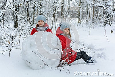 Two twin girls in red jackets rolling huge snowball to make snowman Stock Photo