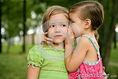 Two twin little sister girls whisper in ear Stock Photo