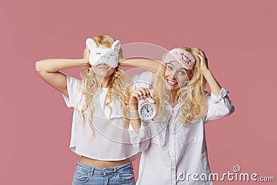 Two twin sleepless young women in pajamas and sleep masks on a pink background. Stock Photo