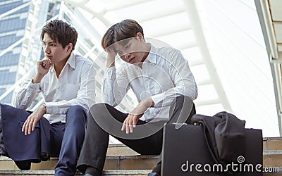 Two unemployed workers sitting beside the street and being sad Stock Photo