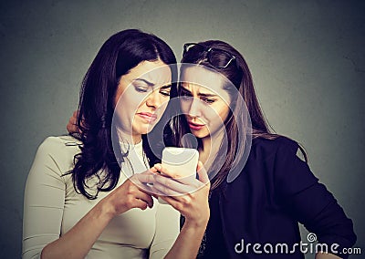 Two upset friends women viewing on line content on a smart phone Stock Photo