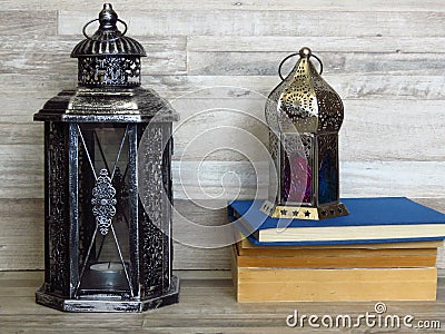 Two very old silver lanterns and a pile of old books on bleached oak background. Stock Photo