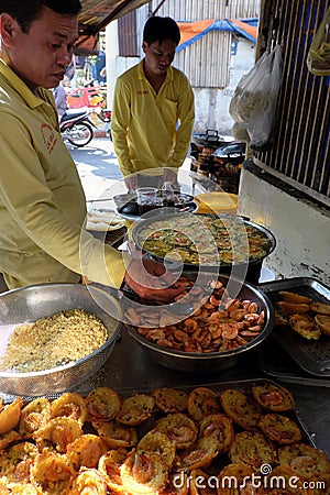 Two Vietnamese man making mini shrimp pancake on pavement at sidewalk restaurant, yellow crispy cake Editorial Stock Photo