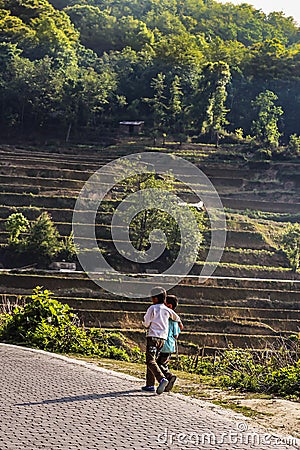 Two village boys walking at the side of a dirty path next to the rice terraces at Yuanyang Editorial Stock Photo