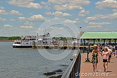 Two visitors are enjoying the day while other visitors are queueing at Liberty Island for Statue Cruises in the background Editorial Stock Photo