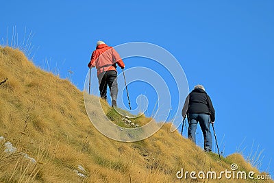 two with walking sticks ascending steep hill, clear day Stock Photo