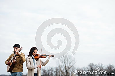 Two warmly dressed musicians playing in countryside at autumn over bright sky Stock Photo