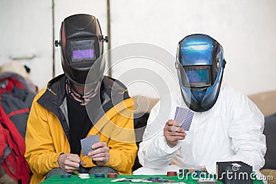 Two welders in welding masks play poker. Editorial Stock Photo