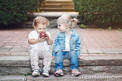 Two white Caucasian cute adorable funny children toddlers sitting together sharing eating apple food Stock Photo