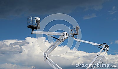 Two white cherry pickers against blue sky with clouds, Under there are fluffy clouds, above dark clouds Stock Photo