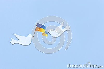 Two white figurines of a doves of peace with flag of Ukraine in their beaks on the light blue background. Peace Concept Stock Photo