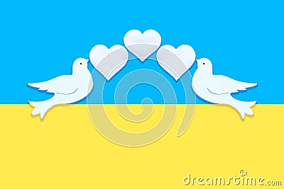 Two white figurines of a doves of peace with hearts in their beaks on the background of the colors of the flag of Ukraine. Concept Stock Photo