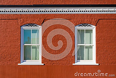 Two white framed windows in a red brick building with scrollwork and cornice Stock Photo