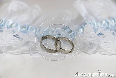 Two white gold wedding rings on white lace pad and blue garter Stock Photo