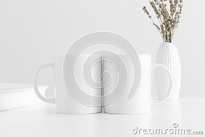 Two white mugs mockup with a lavender in a vase and a book on a white table Stock Photo