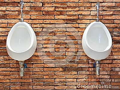 two white urinal for male decoration on oramge bricks wall . public install urine flush Stock Photo