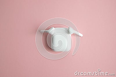 Two white wireless earphones lying on the sides of the closed charger. Pink background. Place for text Stock Photo