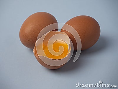 Two whole raw brown chicken eggs and a broken half egg with yellow yolk closeup on a blue background Stock Photo
