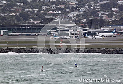 Two wind surfers on Lyall Bay in Wellington New Zealand on a grey stormy day. The airport can be seen in the background Editorial Stock Photo