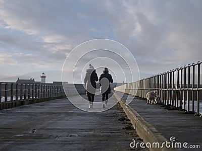 Two woman in dark warm clothes walking their pet dogs by ocean. Concept outdoor activity, socializing Editorial Stock Photo