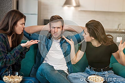 Two women arguing with their friend man sitting together on the sofa, opposite sexes concept Stock Photo
