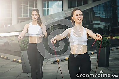 Two women athletes jumping on skipping ropes in city street. Girls train outdoors. Workout, sports, healthy lifestyle. Stock Photo