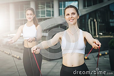 Two women athletes jumping on skipping ropes in city street. Girls train outdoors. Workout, sports, healthy lifestyle. Stock Photo