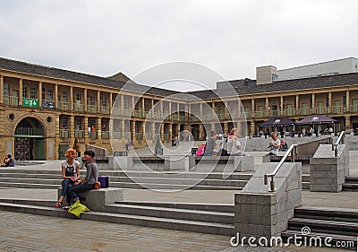 Two women in conversation sat on the steps of the piece hall in halifax west yorkshire with people shopping and sat in cafes and Editorial Stock Photo