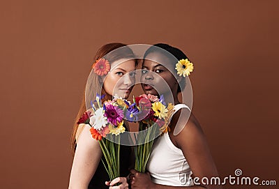 Two women of different races with flowers in their hairs holding bouquets. Caucasian and African American females looking at Stock Photo