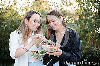 Two women friends eating fresh salads in bowls outdoor together. Stock Photo