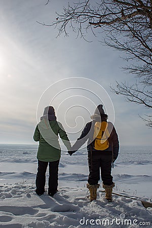 Two woman holding hands with backs turned on frozen lake shore p Stock Photo