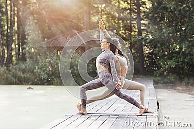 Two women holding hands perform virabhadrasana exercise, the first warrior pose, doing yoga Stock Photo