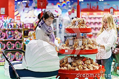 Two women like gay couple or friends with white baby carriage is looking for some toy bear in the big colorful supermarket Stock Photo