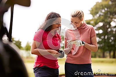 Two Women Playing Golf Marking Scorecard With Buggy In Foreground Stock Photo