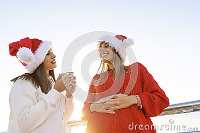 Two women in Santa Claus hat having bonding outdoor holding a Christmas tea mug - Bottom view of beautiful woman leaning to a Stock Photo