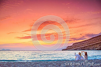 Two women taking photos of the amazing sunset at the beach of Matala, Crete Editorial Stock Photo