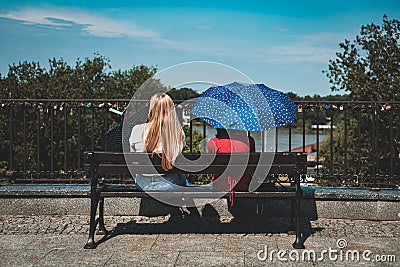 Two women with umbrellas sitting on a bench Editorial Stock Photo