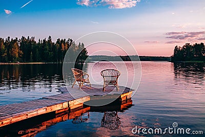 Two wooden chairs on a wood pier overlooking a lake at sunset Stock Photo