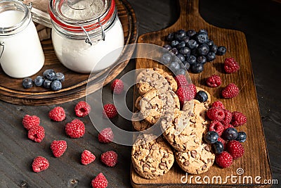 Two wooden platters with chcocolate biscuits, raspberries, blueberries, milk and flour. Stock Photo