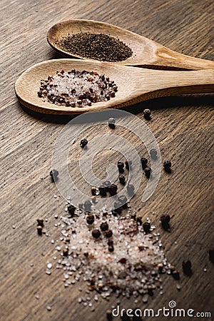 Two wooden spoons with salt and pepper on a wooden table Stock Photo