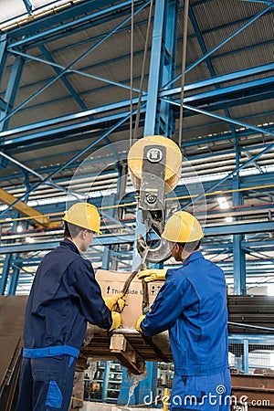 Two workers handling heavy loading lifted by crane Stock Photo