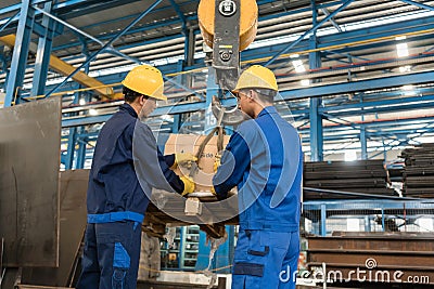 Two workers handling heavy loading lifted by crane Stock Photo