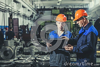 Two workers at an industrial plant with a tablet in hand, working together manufacturing activities Stock Photo