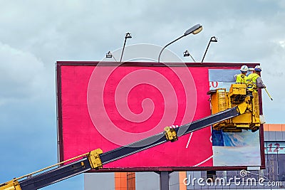 Two workers install red billboard on roadside of city street Editorial Stock Photo